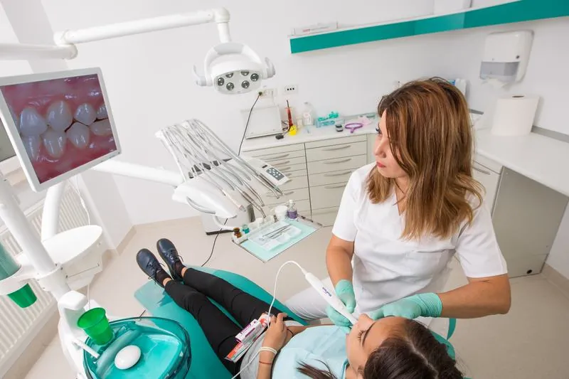 Sala de tratament a cabinetului, cu fotoliul dentar și monitorul pe care medicul arată pacientei imaginile dinților