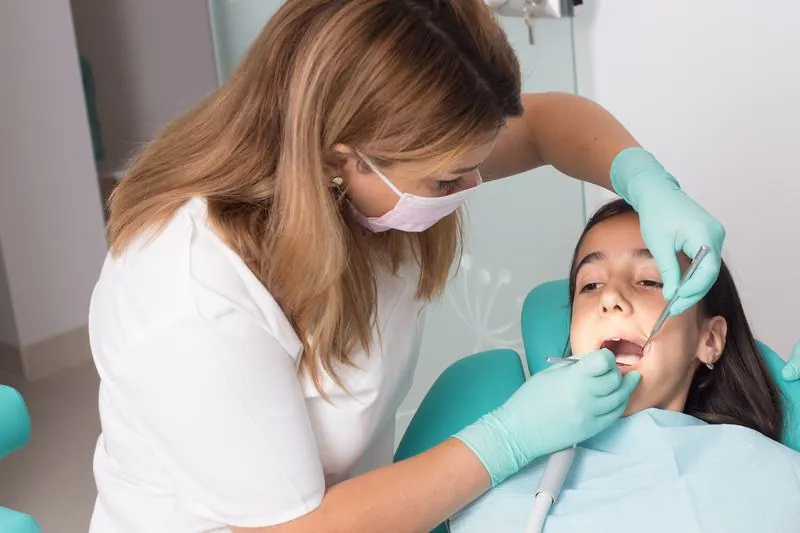 Medicul examinează dinții unei paciente tinere, așezată în fotoliul dentar